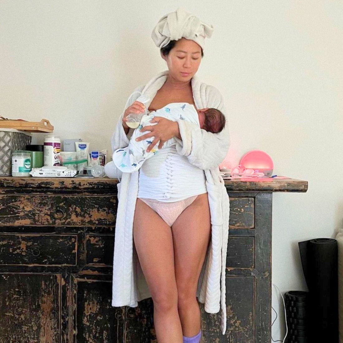 Postpartum mom with belly wrap holding her baby with good posture preventing back pain