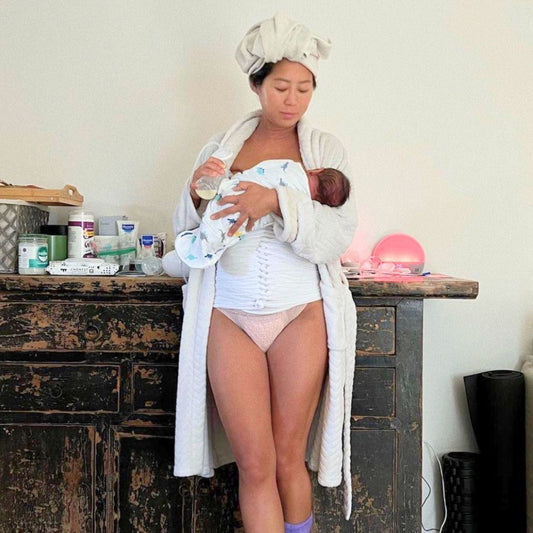 Postpartum mom with belly wrap holding her baby with good posture preventing back pain