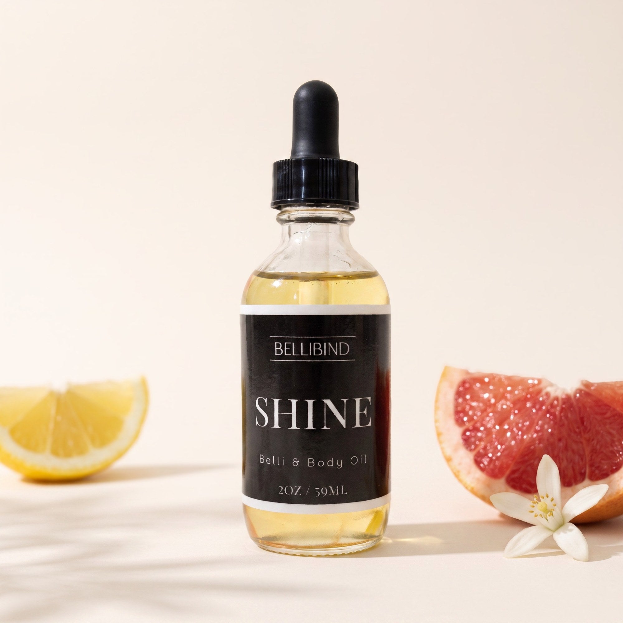 Bellibind Shine Belli and Body Oil in a glass dropper bottle beside lemon, grapefruit and neroli blossom.