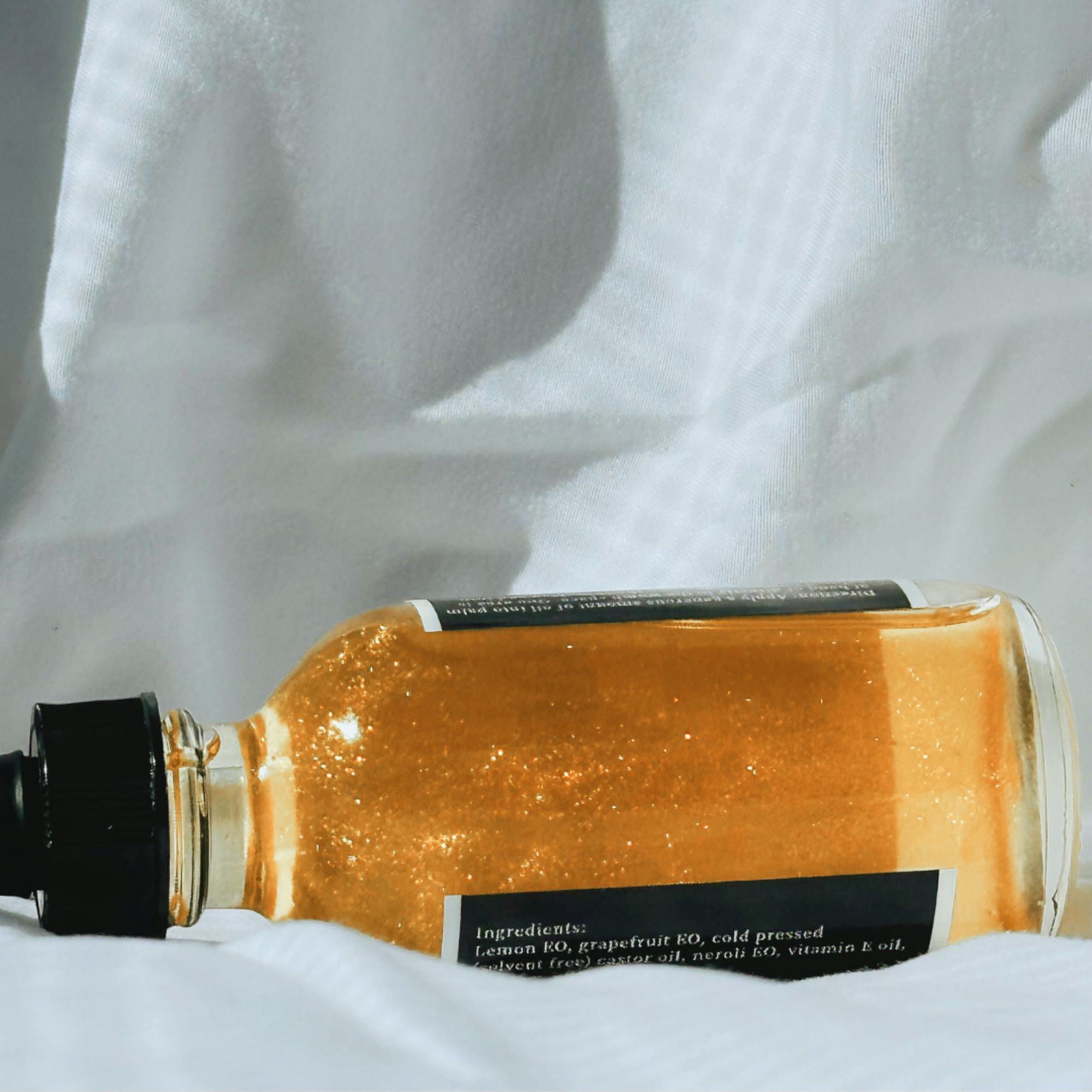 Real 24k gold dust suspended in Bellibind Shine Belli and Body Oil, shown against white linen.